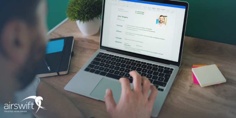 A man browses a resume on a laptop, sitting in a green-walled office